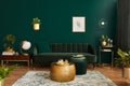 Luxury living room in house with modern interior design, green velvet sofa, coffee table, pouf, gold decoration, plant, commode. Royalty Free Stock Photo