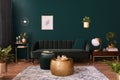 Luxury living room in house with modern interior design, green velvet sofa, coffee table, pouf, gold decoration, plant, commode. Royalty Free Stock Photo