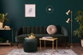 Luxury living room in house with modern interior design, green velvet sofa, coffee table, pouf, gold decoration, plant, lamp. Royalty Free Stock Photo