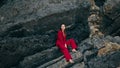 Luxury model sitting rock wearing stylish red suit. Woman posing on stone cliff Royalty Free Stock Photo