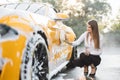 Young woman in business outfit, shirt and trousers using yellow sponge for cleaning car door Royalty Free Stock Photo