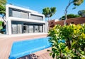 Luxury modern white house with large windows overlooking a Mediterian landscaped garden with palm trees and  blue swimming pool. Royalty Free Stock Photo