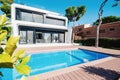 Luxury modern white house with large windows overlooking a Mediterian landscaped garden with palm trees and  blue swimming pool. Royalty Free Stock Photo