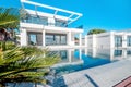 Luxury modern white house with large windows overlooking a Mediterian landscaped garden with palm trees and  blue swimming pool. Royalty Free Stock Photo