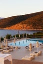 Luxury morning swimming pool with empty deck chairs, tables and umbrellas at the resort with beautiful sea view. Greek Royalty Free Stock Photo