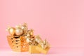 Luxury New Year gold shimmer decor with Christmas stars, balls with ribbon in bowl, present on soft light pink background.