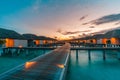 Luxury over water villas warm orange led lights, bungalows sea ocean with beach at night sunset time Royalty Free Stock Photo