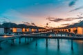 Luxury over water villas warm orange led lights, bungalows sea ocean with beach at night sunset time Royalty Free Stock Photo