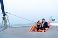 Luxury relaxing couple traveler in nice dress and suite sit on bean bag and drink a glass of wine in part of cruise yacht with Royalty Free Stock Photo