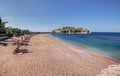 Sand beach with wooden chaise-longue chairs and umbrellas near the Sveti Stefan historical town on the island. Montenegro Royalty Free Stock Photo