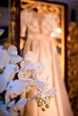 Luxury satin and lace wedding dress hanging on a gold carved screen against the background of orchids Royalty Free Stock Photo