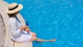luxury senior woman dangling her legs in an outdoor swimming pool holding a blue refreshing cocktail wearing a straw hat Royalty Free Stock Photo