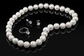 Luxury set white pearl necklace and jewelry with diamonds in ring and earrings on a black background with glossy reflection Royalty Free Stock Photo