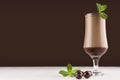 Luxury sweet chocolate cocktail in elegant glass with fresh green mint and with round chocolate candies on dark brown background.