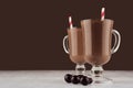 Luxury sweet chocolate dessert in irish coffee glass with round chocolates and red striped straw on dark brown background.