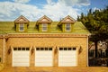 Luxury three car garage with carriage lights between doors set in brick house with green wood shingle roof and dormers