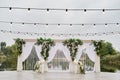 Luxury wedding arch decorated with palm leaves, orchid flowers, floral peacocks and bulbs garland outdoors, copy space.