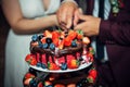 Luxury wedding cake decorated with chocolate, icing, fresh berries. Newlywed cut big beautiful cake at a wedding banquet, close-up