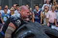 LVIV, UKRAINE - AUGUST 2017: A super strong athlete raises a huge Good year wheel at competitions in front of enthusiastic spectat