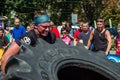 LVIV, UKRAINE - AUGUST 2017: A super strong athlete raises a huge Good year wheel at competitions in front of enthusiastic spectat
