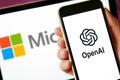 Lviv, Ukraine - 03 11 2023: hand holding smartphone with OPENAI logo on screen and laptop display with MICROSOFT logo