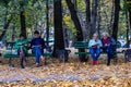 Two couples sit on park benches: young people read books, seniors use smartphone.