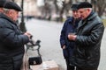 Lviv, Ukraine, 03.18.2019, three elderly men stand in a park near a bench and play card games