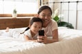 Lying in bed asian mother show daughter cartoons on smartphone