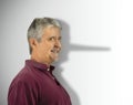 Lying dishonest man with his growing long liar Pinocchio nose showing in his shadow Royalty Free Stock Photo