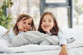 Lying down on bed and looking at the camera. Two cute little girls indoors at home together. Children having fun Royalty Free Stock Photo