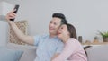 While lying on the sofa at home, a happy young couple uses their phone and converses with each other