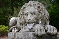 Lying stone lion statue, staring forward, placed on stone pedestal