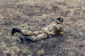 Lying Ukrainian soldier disguises in steppe against of background of dry grass