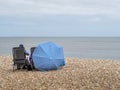 LYME REGIS, DORSET, UK - MAY 7 2023: The epitome of an English summer as couple hunker down under beach umbrella in