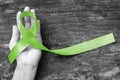 Lymphoma Cancer Awareness Lime Green color ribbon on helping hand on old aged wood background: Satin fabric symbolic logo raising