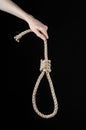 Lynching and suicide theme: man's hand holding a loop of rope for hanging on black isolated background