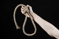 Lynching and suicide theme: man's hand holding a loop of rope for hanging on black isolated background