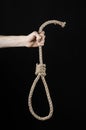 Lynching and suicide theme: man's hand holding a loop of rope for hanging on black isolated background