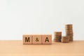 M and A, Mergers and Acquisitions, text on wooden cube blocks with blurred stack of coins including copy space Royalty Free Stock Photo