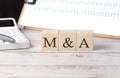 M and A word on a wooden block with clipboard and calculator