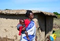 Maasai woman with a baby in her arms walks in the middle of a typical Maasai village