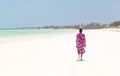 Maasai warrior walking on picture perfect tropical sandy beach. Paje, Zanzibar, Tanzania.
