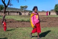 Maasai woman with a child walks in the middle of a typical Maasai village