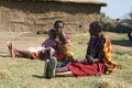 Maasai women with an unidentified baby rest in front of a mud built hut.