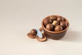 Macadamia nuts in ceramic bowl on beige background. Nuts with sawn nutshells and with opener key on the wooden spoon. Healthy