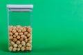 Macadamias inside a transparent plastic container with a green background Royalty Free Stock Photo