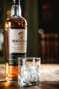 The Macallan whiskey bottle and glass with ice cubes on wooden t