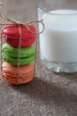 Macarons three pieces red, green, orange tied with rope and glass with milk on burlap tablecloth Royalty Free Stock Photo