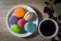 Macarons on white dish with black Coffee in a cup and coffee beans on wood table background