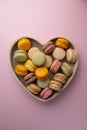 Macaroons colorful cookies in wooden heart bowl. Macarons french sweet dessert, top view, pink background. Copy space Royalty Free Stock Photo